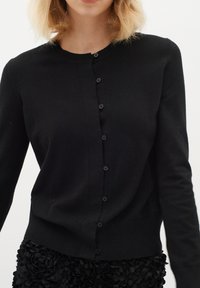 Cardigan nero con scollo rotondo, maniche lunghe e chiusura a bottoni. Tessuto morbido con una leggera elasticità e un design aderente.