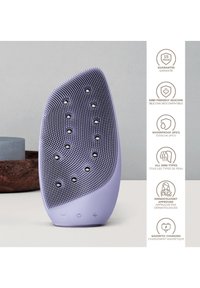 Silicon ansiktsrengöringsapparat i lavendel med texturerad yta, som har upphöjda knölar, en böjd form och tre kontrollknappar i botten.