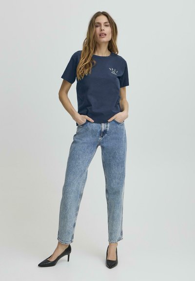 Námořnické bavlněné tričko s kulatým výstřihem a krátkými rukávy, kombinované s světle modrými džínami s vysokým pasem a černými špičatými podpatky.