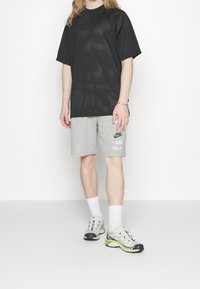 Svart mesh T-shirt med lös passform, grå shorts med Nike-logga och grå sportskor med färgglada detaljer och snören, vita ankelstrumpor.