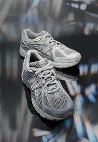 Gray athletic shoes with mesh upper, cushioned soles, textured accents, and logo detail. Features lace-up closure and rounded toe design.