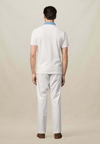 Weiße Polohemd mit einem hellblauen Kragen, kombiniert mit weißen Hosen und braunen Schuhen. Der Stoff wirkt glatt und leicht.
