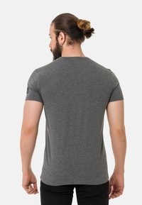 Graues T-Shirt mit kurzen Ärmeln aus weichem Stoff, mit Rundhalsausschnitt und einem kleinen Logo-Patch am linken Ärmel.