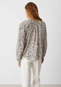 Lightweight, cream-colored blouse with black swirling pattern, long puffed sleeves, and gathered detail at the back neckline.