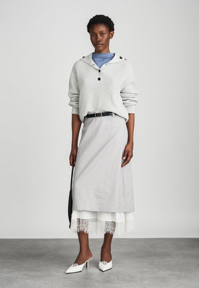 Svetlo sivi pleteni pulover s kapuco in črnimi gumbi, v kombinaciji s svetlo sivim krilom z čipkastim robom in belimi petnimi natikači.