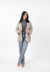 Cárdigan beige claro con punto texturizado, grandes botones y dos bolsillos frontales. Combinado con unos vaqueros de pierna recta de tiro alto y en tonos azules desvaídos.