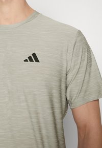 Ljusgrå tränings T-shirt med texturerad tyg, försedd med en svart diagonal randlogotyp på bröstet och rundad halsringning.