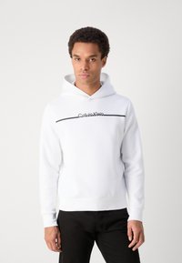 Hanorac alb din material moale, cu o dungi orizontale negre și logo-ul "Calvin Klein" pe piept. Manșete și tiv împletite.