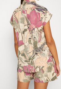 Ærmeløs skjorte og shorts sæt med pink, grøn og beige botanisk print, der præsenterer zebraer og andre dyremotiver på stoffet.
