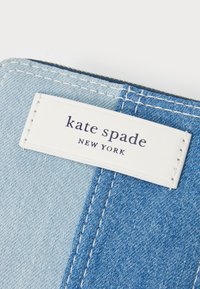 Denim wallet featuring light and dark blue segments, white stitching, and a white label with "kate spade NEW YORK" embossed in dark text.