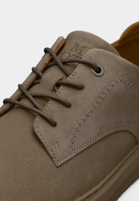 Κοντινή λήψη σε παπούτσι ταούπ από σουέντ με κορδόνια, λεπτομερείς ραφές και ανάγλυφη σήμανση στην γλώσσα.