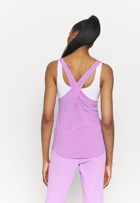 Top sportivo viola con design a incrocio sulla schiena, indossato sopra una canotta bianca. Tessuto liscio, abbinato a pantaloni viola coordinati.