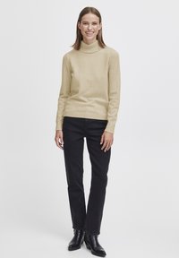 Beige polotröja och svarta raka jeans. Tröjan har en ribbad halsringning och manschetter, och outfiten kompletteras av svarta ankelstövlar.