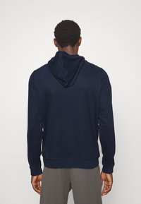 Tumši zilas krāsas kapuce ar mīkstu tekstūru, garām piedurknēm un ribotu apakšmalu. Iezīmē vienkāršu dizainu bez redzamām rakstiem vai piederumiem.