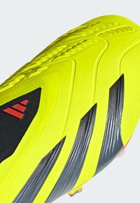 Chaussure de football jaune vif avec des accents en textile noir et trois rayures rouges. Elle présente une surface texturée et une semelle extérieure rayée pour une meilleure traction.