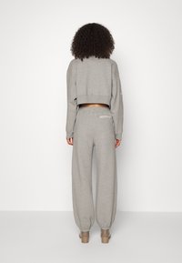 Grå kortärmad sweatshirt med långa ärmar som är matchad med joggers i avslappnad passform och elastiska cuffs, visad bakifrån.