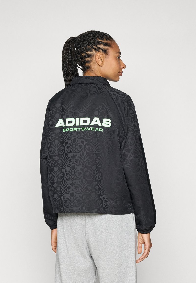 Svart Adidas sportjacka med strukturerat blommönster, utrustad med en limegrön logotyp på baksidan och elastiska ärmslut.