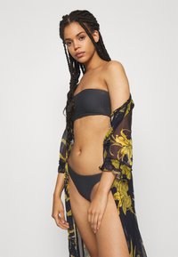 Melnas bandeau bikini top un atbilstošas augstās sēžamvietas bikses, apvienotas ar caurspīdīgu ziedu kimono melnbaltās un dzeltenās krāsās.