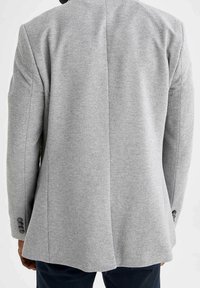 Blazer gris con una tela texturizada, con una abertura en la parte trasera y detalle de tres botones en las mangas. Silueta de corte recto.
