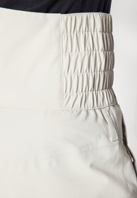 Hellebeige Hose mit einem breiten, gerafften Bund. Der Stoff wirkt strukturiert und zeigt eine glatte Oberfläche mit einem Seitentaschen-Detail.
