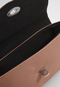 Piccolo borsetta in pelle rosa pallido con interno in tessuto nero e chiusura in argento, mostrata aperta e vuota su uno sfondo bianco.