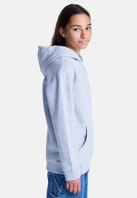 Felpa in cotone grigia con tasca a canguro e polsini a costine, abbinata a jeans in denim blu. La felpa presenta un cordino e un design semplice.