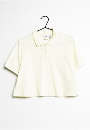Skrócona żółta koszulka polo z miękkiej bawełny, z trzema guzikami na stójce i białym logo po lewej stronie klatki piersiowej. Krótkie rękawy.