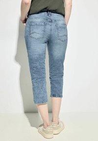 Light blue denim cropped jeans with a faded texture and two back pockets. Paired with light beige sneakers.
