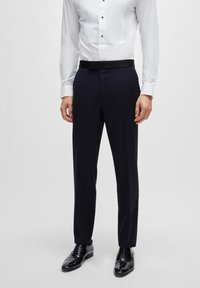 Marineblaues Anzughosen mit glatter Oberfläche. Mit flachem Vorderteil, taillierter Passform und schwarzem Bund, kombiniert mit glänzenden schwarzen Schuhen.