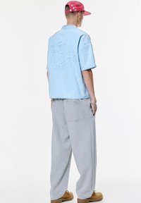 Cămașă scurtă de culoare bleu deschis, cu broderie în formă de stea pe spate, asortată cu pantaloni de trening gri, largi, și pantofi slip-on de culoare bej. Capac cu model de stele roz.