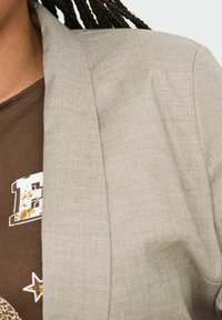 Helehall hall särk, mis on valmistatud tekstuurilisest kangast, millel on vabalt langev lõige ja šaalikaelus, kantud pruunilt graafiliselt T-särgilt.