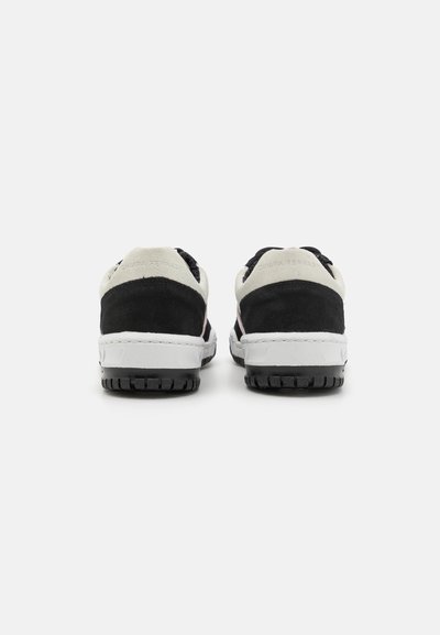 Ein Paar schwarz-weiße Sneakers mit dicken weißen Sohlen, von hinten auf einem schlichten weißen Hintergrund gezeigt.