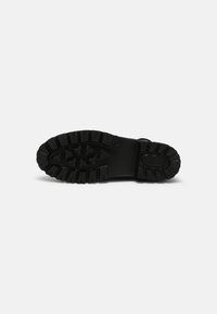 Suela de zapato de goma negra con un patrón de tracción profundo y acentos triangulares elevados, que presenta una textura suave y bordes redondeados.