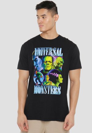Man wearing black t-shirt featuring colorful portraits of Universal Monsters characters on a plain background.