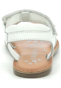 Sandale en cuir blanc avec une semelle marron. Elle dispose d'une sangle Velcro, d'un semelle intérieure rembourrée et d'un motif floral gravé sur la semelle.