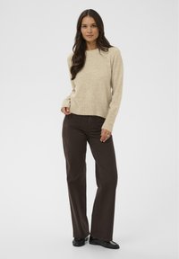 Suéter de punto beige con mangas largas y dobladillo acanalado, combinado con pantalones rectos marrón oscuro y mocasines negros de charol.