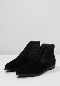 Bottines noires en daim avec un dessus en daim, un panneau latéral texturé, un bout pointu et une fermeture à lacets à six œillets. Semelle plate.