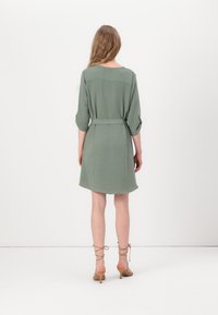 Vestido verde de mangas curtas com cintura cingida; textura suave, barra arredondada e um corte solto. Design simples e minimalista.