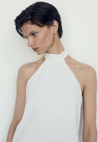 Top alb cu gât halter, cu o textură netedă și mată. Designul simplu are un decolteu înalt și umeri expuși, creând o siluetă curată.