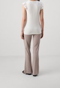 Top blanco con mangas acampanadas, combinado con pantalones acampanados de canalé marrón claro. La modelo lleva sandalias negras. Fondo sencillo.