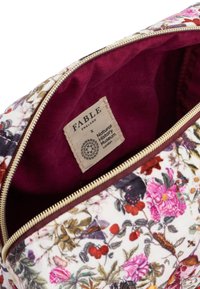 Borsa cosmetica floreale con esterno in tessuto bianco, foderata in bordeaux, caratterizzata da una zip dorata. L'etichetta recita "FABLE" e "Museo di Storia Naturale."