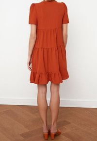 Rostfarbiges kurzärmliges Kleid mit einem gestuften Rüschensaum, aus strukturiertem Stoff, mit einer taillierten Oberteil und entspanntem Schnitt.