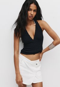 Zwart textuur crop top met een diepe V-hals, gecombineerd met witte shorts in rokstijl met een knoopsluiting en een zijslit.