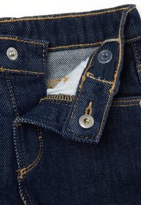 Jeans de mezclilla azul oscuro con un botón de metal y cierre de botón a presión, que presentan costuras visibles y un tejido texturizado.