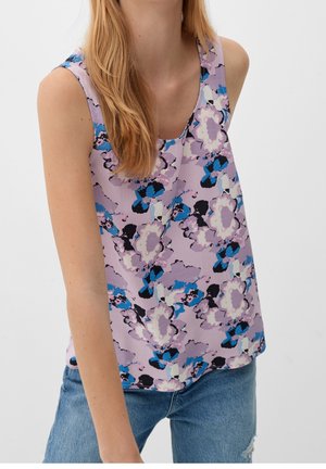 Mujer que lleva una camiseta de tirantes lavanda con un gran estampado floral azul, negro y blanco combinada con vaqueros azules.