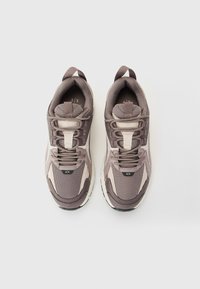 O pereche de sneakers gri și bej Armani Exchange, cu detalii din plasă și suede, cu șireturile legate, văzuți dintr-o perspectivă de sus pe un fundal alb.