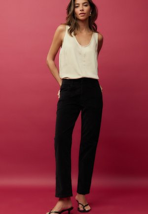 Pantalons noirs en coton avec une jambe droite et des poches avant, associés à un haut sans manches beige clair. Texture lisse, détails minimaux.