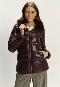 Burgunderfarbene Pufferjacke mit einem plüschigen Kragen, Reißverschluss und horizontaler Steppung. Verfügt über Seitentaschen und eine glänzende Oberfläche.