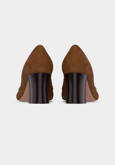 Paire d'escarpins en suède marron avec talons blocs arrondis, vus de dos sur un fond blanc.