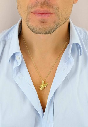Collana con pendente a forma di aquila in oro, indossata su una camicia colletto azzurro chiaro. L'aquila presenta ali dettagliate e una superficie testurizzata.